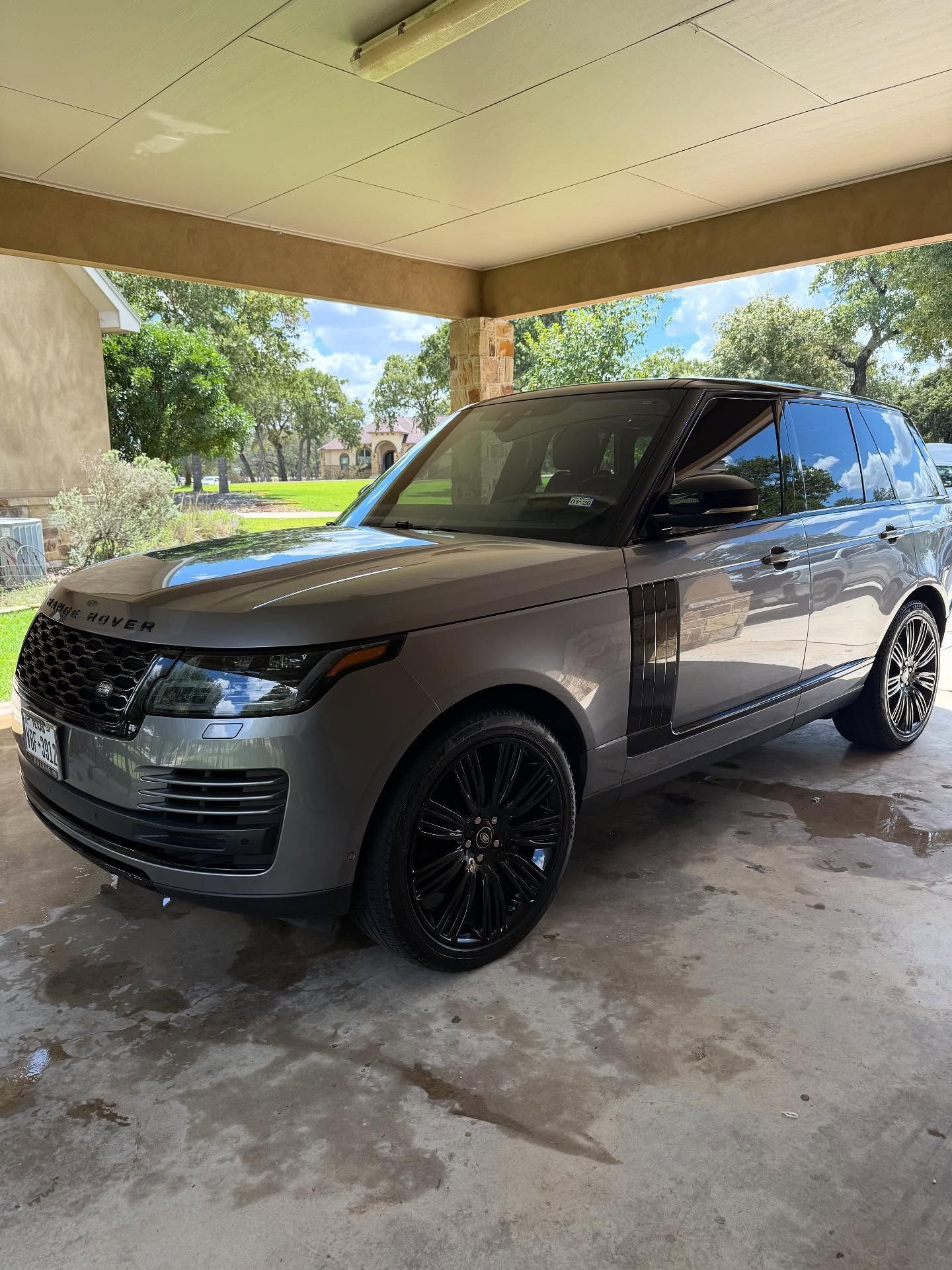 Gray SUV parked under a carport, with black wheels and tinted windows, on a wet driveway