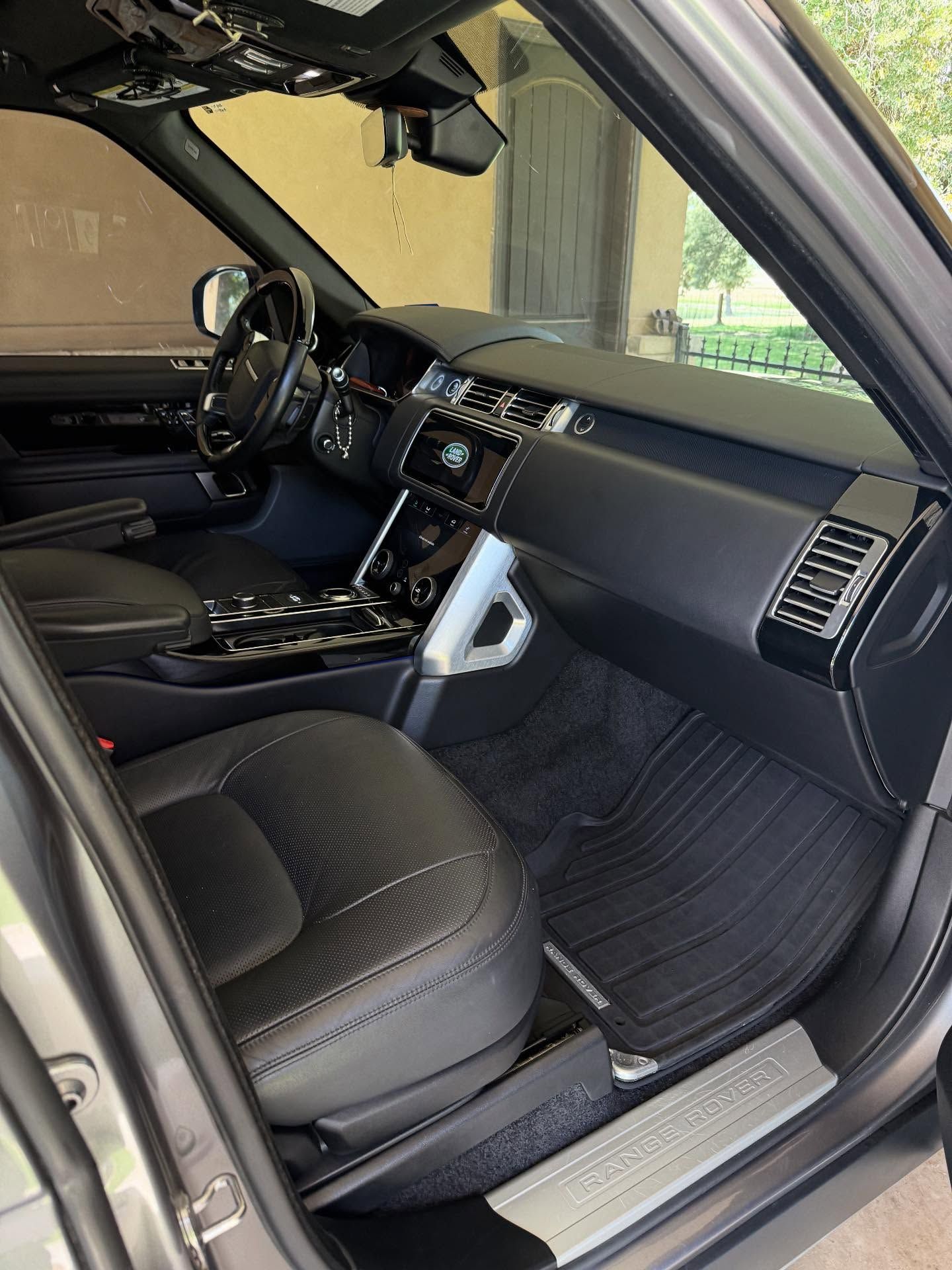 Black leather car interior with open driver door, dashboard, center console, and front seat visible