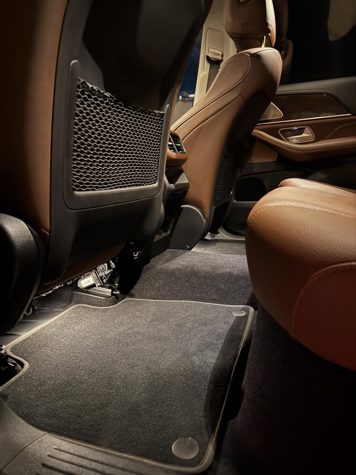 Car interior with brown leather seats, floor mats, and a mesh pocket on the back of the front seat