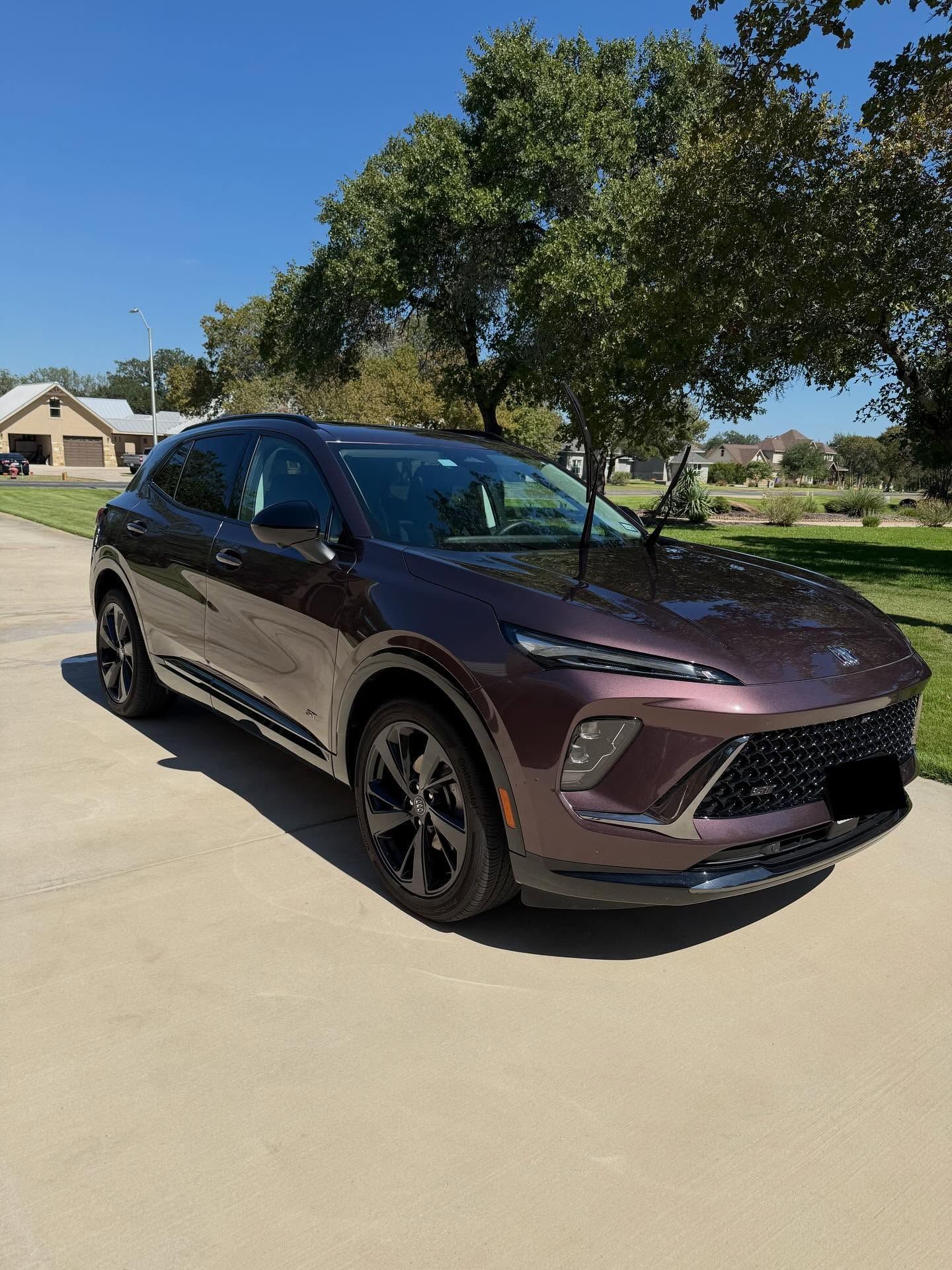 Maroon SUV parked in a driveway on a sunny suburban street with a tree overhead
