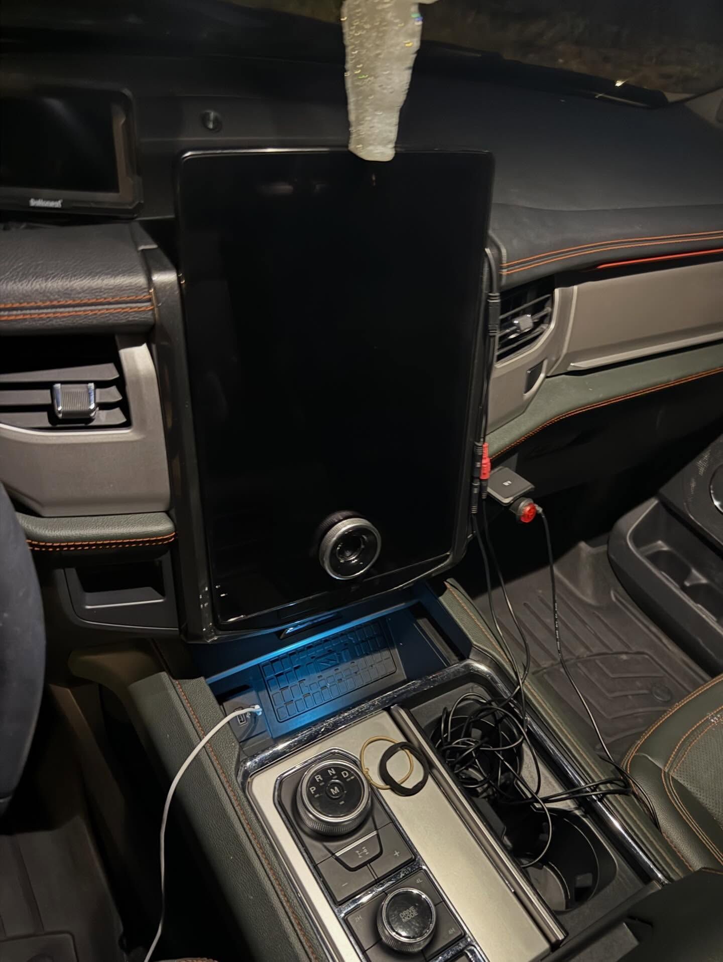 Car interior with a large black touchscreen mounted over the center console, illuminated in blue.