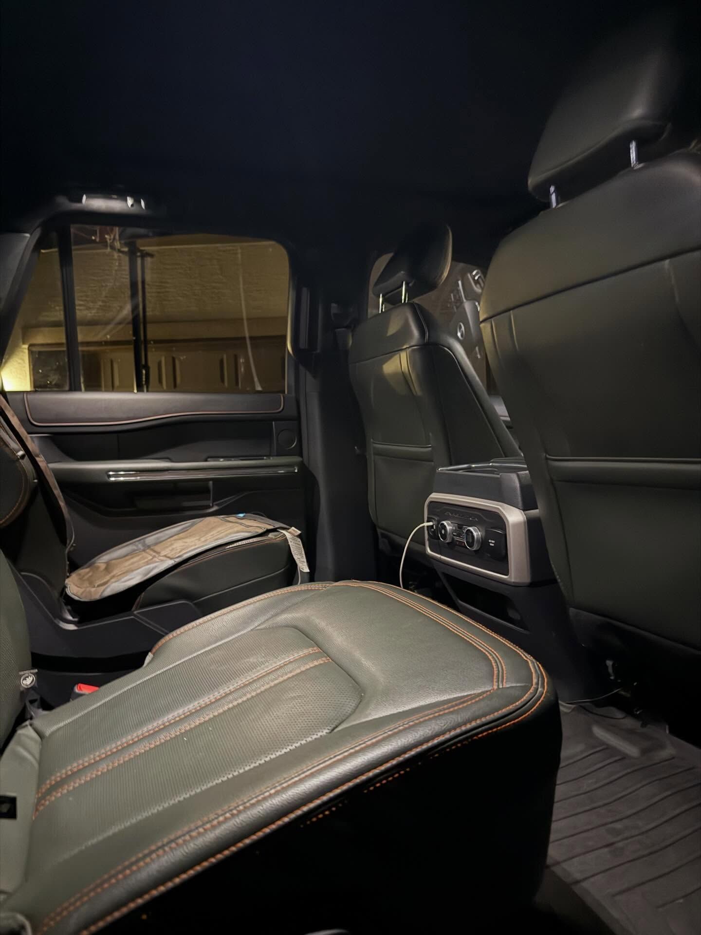 Black leather car interior with rear seats and center console, viewed from the back seat