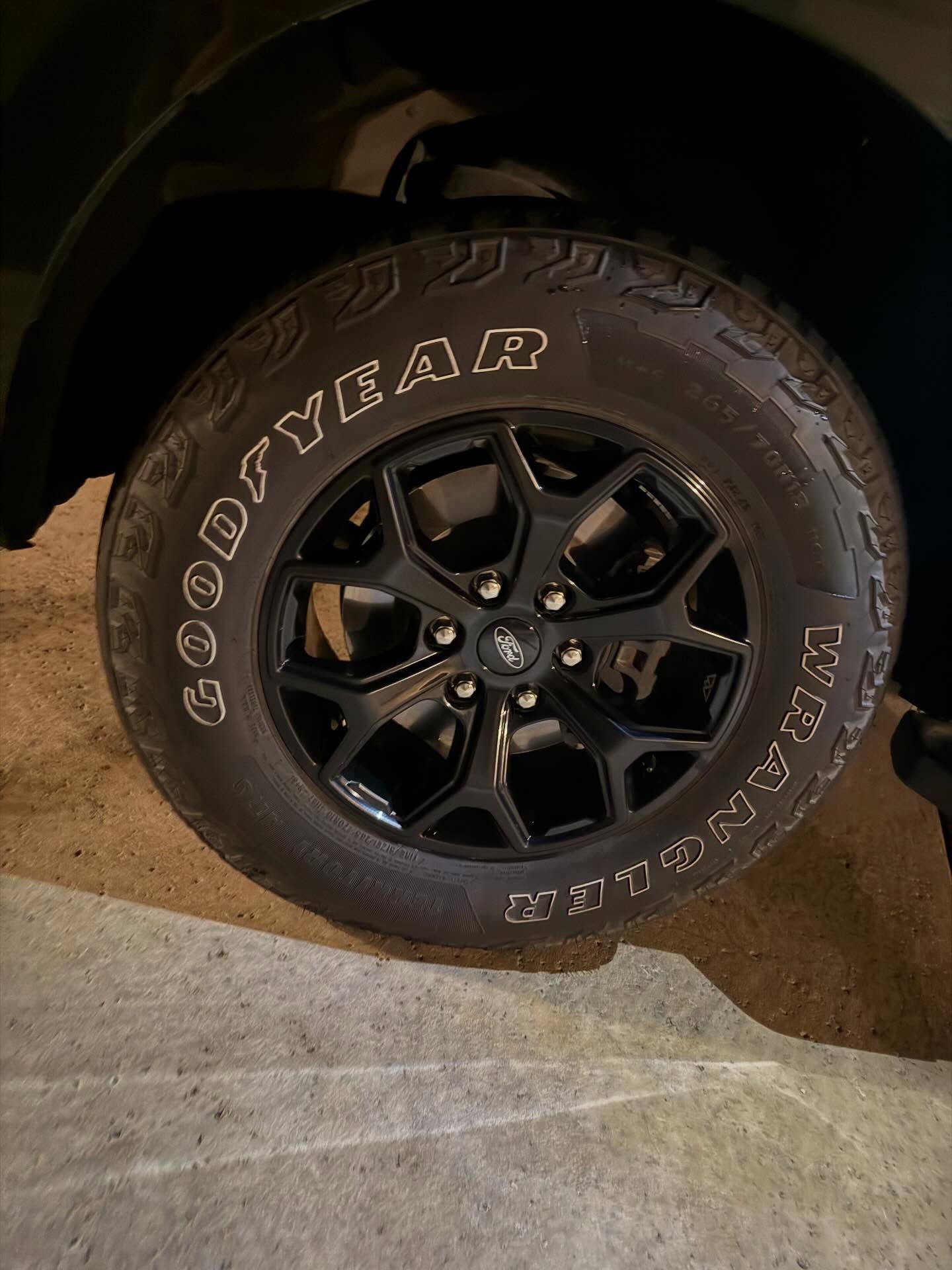 Close-up of a black Goodyear tire and wheel on a vehicle parked on a concrete surface.