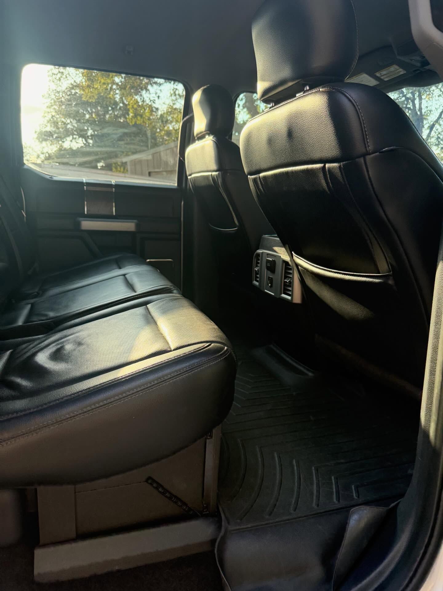 Black leather car back seat interior with sunlight through the window and rear air vents visible