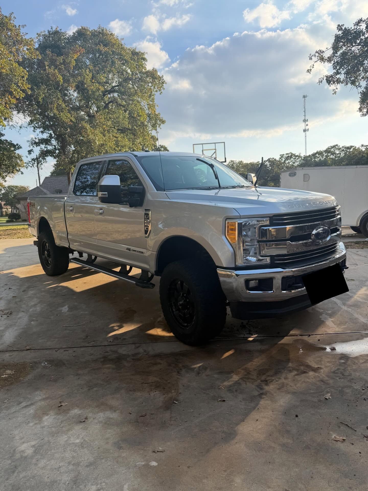 Silver pickup truck parked on a wet road under trees and a partly cloudy sky