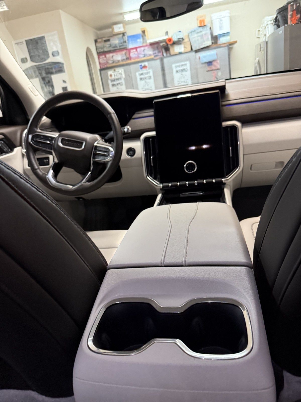 Front interior of a luxury car, showing black-and-beige seats, center console cupholders, and steering wheel.