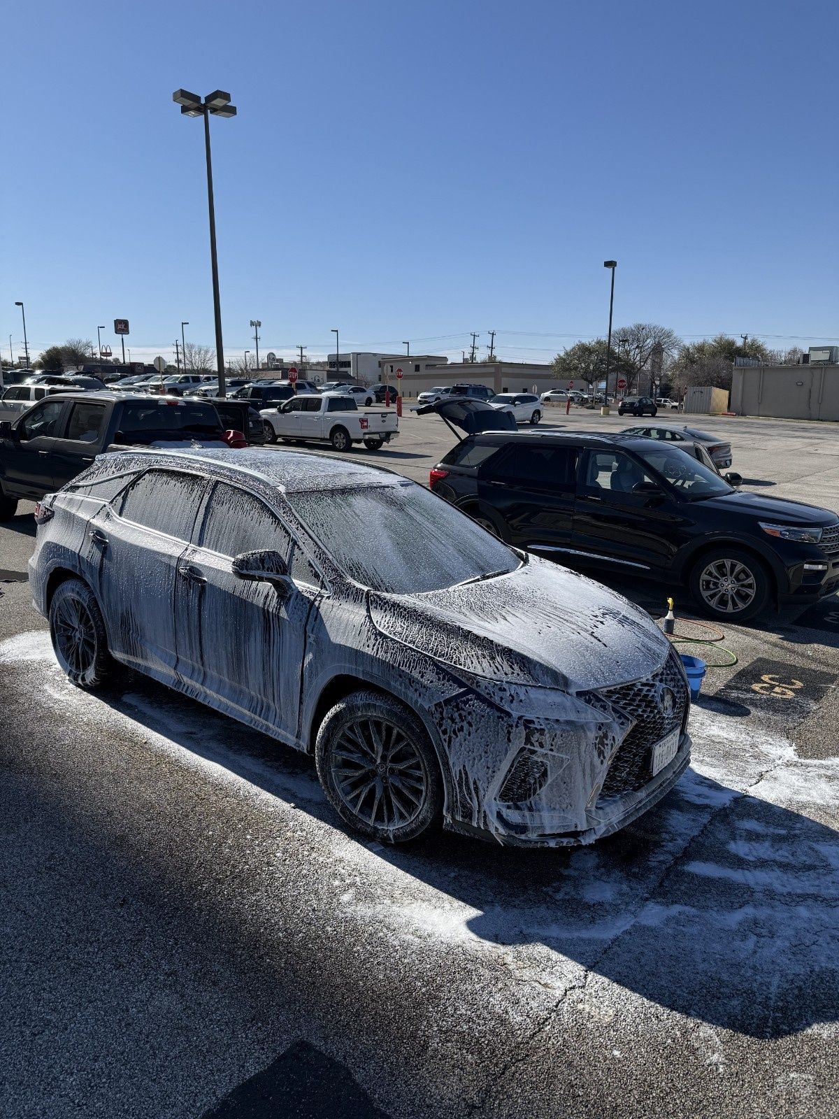 Foam-covered silver car in a parking lot on a sunny day