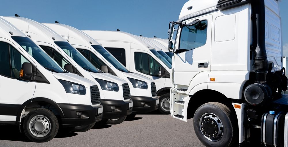Row of white delivery trucks parked in a lot under a clear blue sky