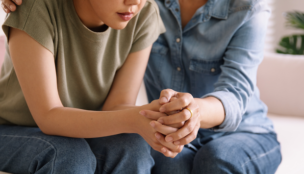 Person comforted, holding hands. One hand on shoulder, soft colors, indoor setting.