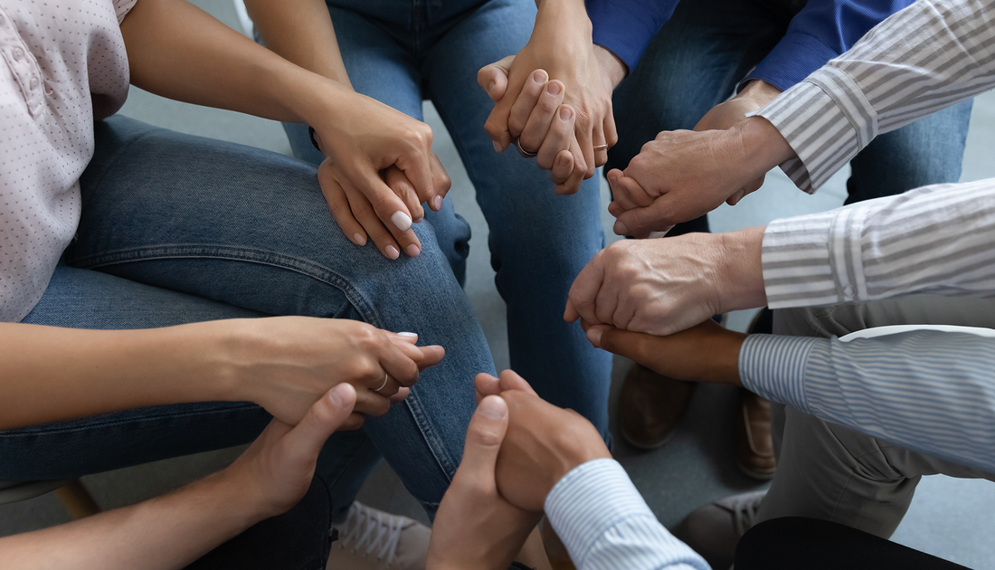 People in a circle holding hands, likely in a support group or counseling session.