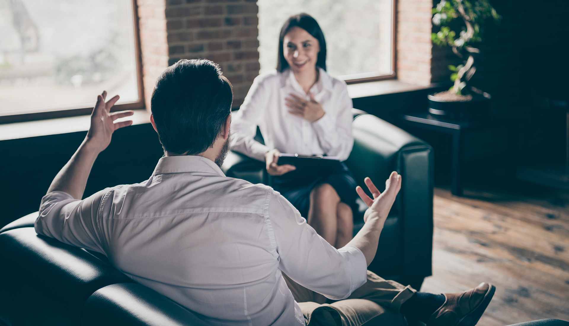 Man gestures while talking to smiling therapist in office setting.