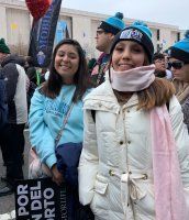 Two smiling people in winter clothes standing in a crowd during a protest