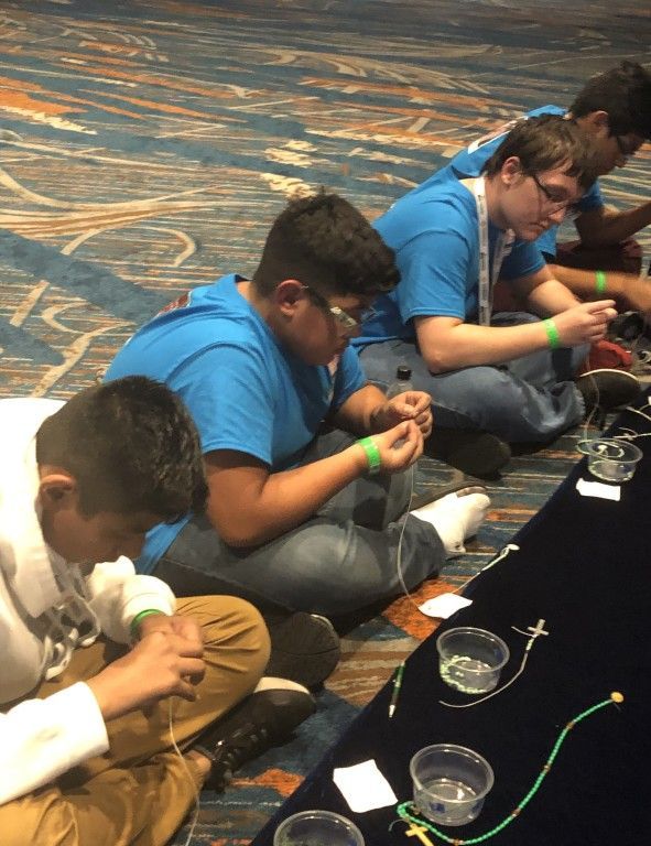 People in blue shirts sit on the floor, working with small objects and cups in a hands-on activity.