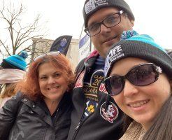 Three people in winter hats and jackets smiling outdoors at a public event