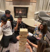 Friends playing giant Jenga on a living room rug by a fireplace