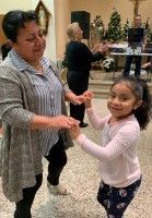 Woman and young girl dancing indoors, smiling and holding hands in a lively room