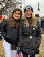 Two people standing outdoors, wearing dark coats and smiling at the camera.