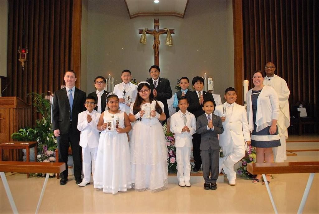 Group posing in a church, with children in white dresses and boys in suits under a cross.