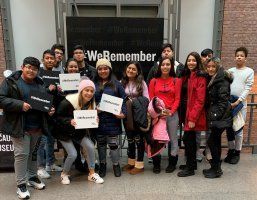 Group of people posing indoors with “We Remember” signs in front of a backdrop.