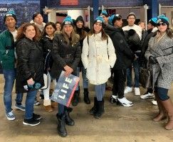 Group of people posing outdoors in winter coats, one holding a LIFE magazine sign.