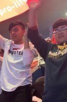 Two people cheering with raised arms in a brightly lit indoor audience area