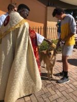 Two people bowing toward a man in a red-and-gold robe outdoors on a brick walkway