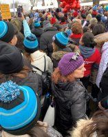 Crowd of people in blue hats at an outdoor event, gathered around bright red balloons