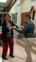 Two people shaking hands in a hallway, smiling and facing each other.