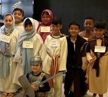 Children in costumes posing on a stage, wearing name tags and smiling