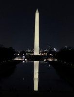 Washington Monument illuminated at night, reflected in the dark water of the Reflecting Pool.