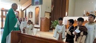 Priest in green vestments speaking to altar servers in a church sanctuary