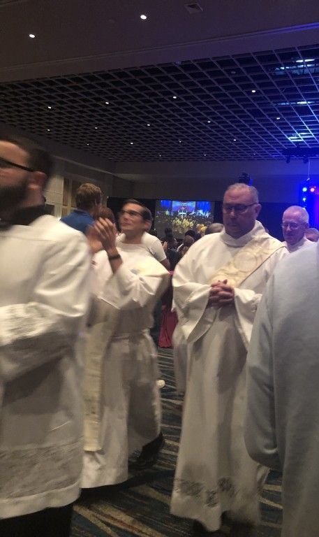 People in white robes walking together indoors under blue lighting