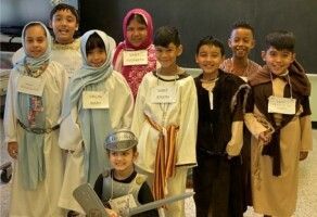 Children in costumes posing indoors, with toy props and name tags, smiling at the camera.