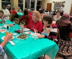 People seated at turquoise-covered banquet tables eating and chatting in a hall