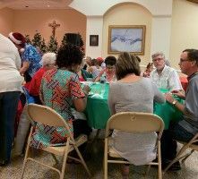 People seated around a table at a community gathering in a beige room with teal tablecloths.