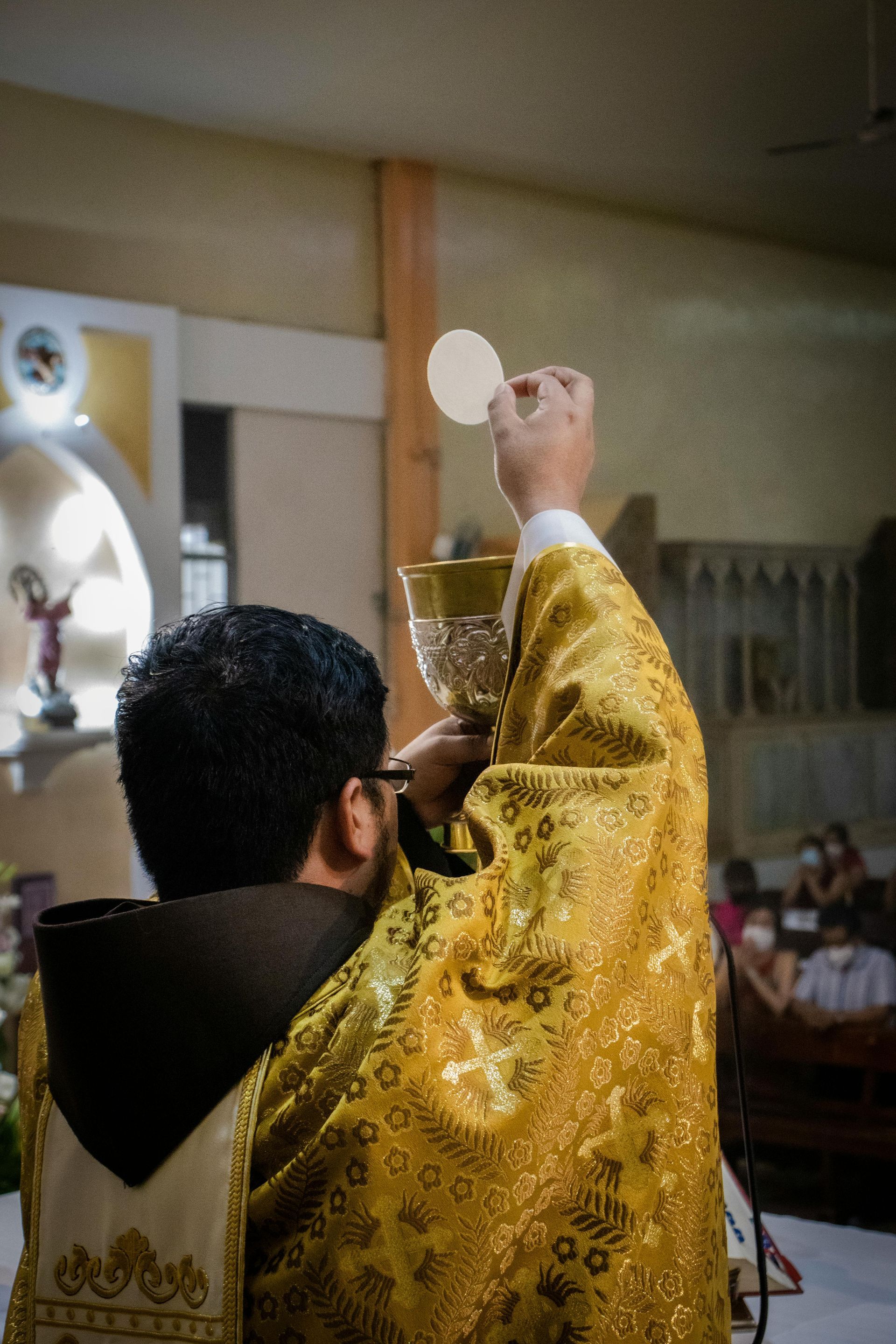 Priest in gold vestments elevates a communion wafer during Mass inside a church