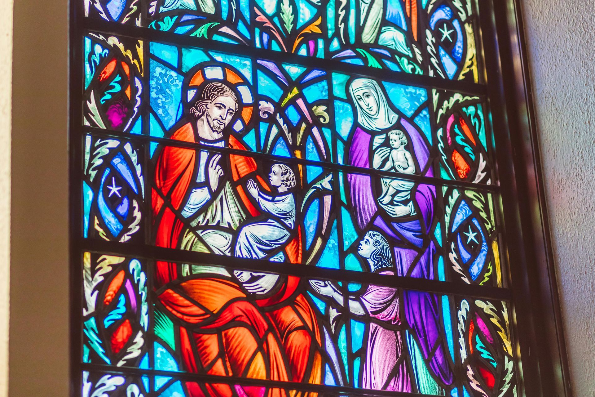 Stained-glass panel of two seated figures in red and purple robes beside a sheep, with blue and gold accents