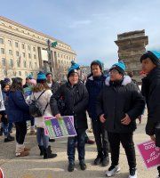 Group of people in blue hats standing outdoors in a city square on a cold day