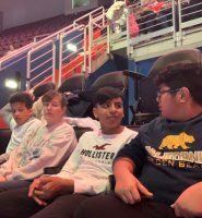 Four people sitting in stadium seats, chatting under colorful arena lights.
