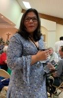 Woman in a patterned dress holding an item indoors, with seated people in the background.