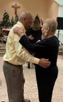 Two people dancing in a church hall with a cross on the wall
