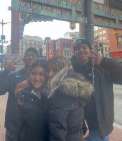 Group of four people posing outdoors under a colorful archway, smiling and huddled close together.