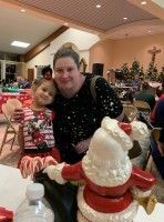 Woman and child posing with Santa in a festive hall, with a Christmas tree and decorations in the background