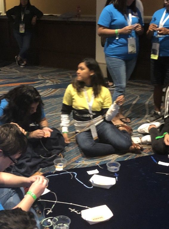 People sitting on the floor in a dim room, talking and using phones with cables scattered around