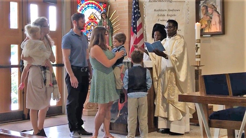 People gathered in a church, greeting a priest near stained glass windows.