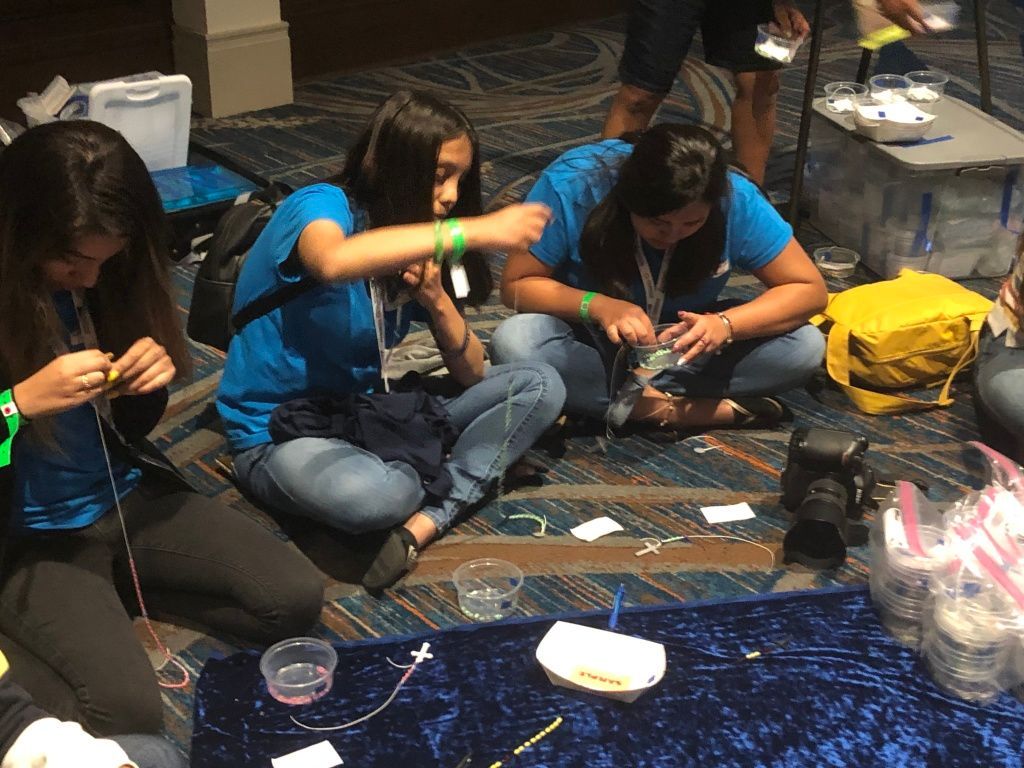 People sitting on the floor, focused on a craft activity with small tools and supplies around them