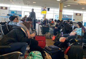 Crowded airport gate with seated travelers and luggage waiting to board