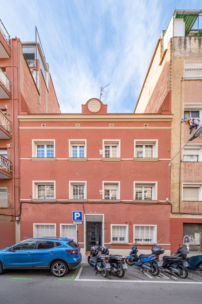 A blue car is parked in front of a red building with motorcycles parked in front of it.