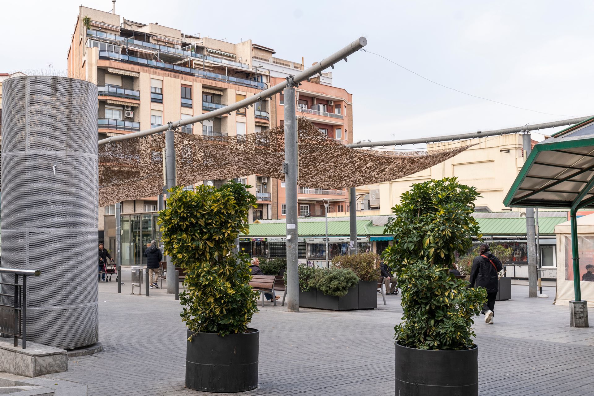 A woman is walking in a park with potted plants and a building in the background