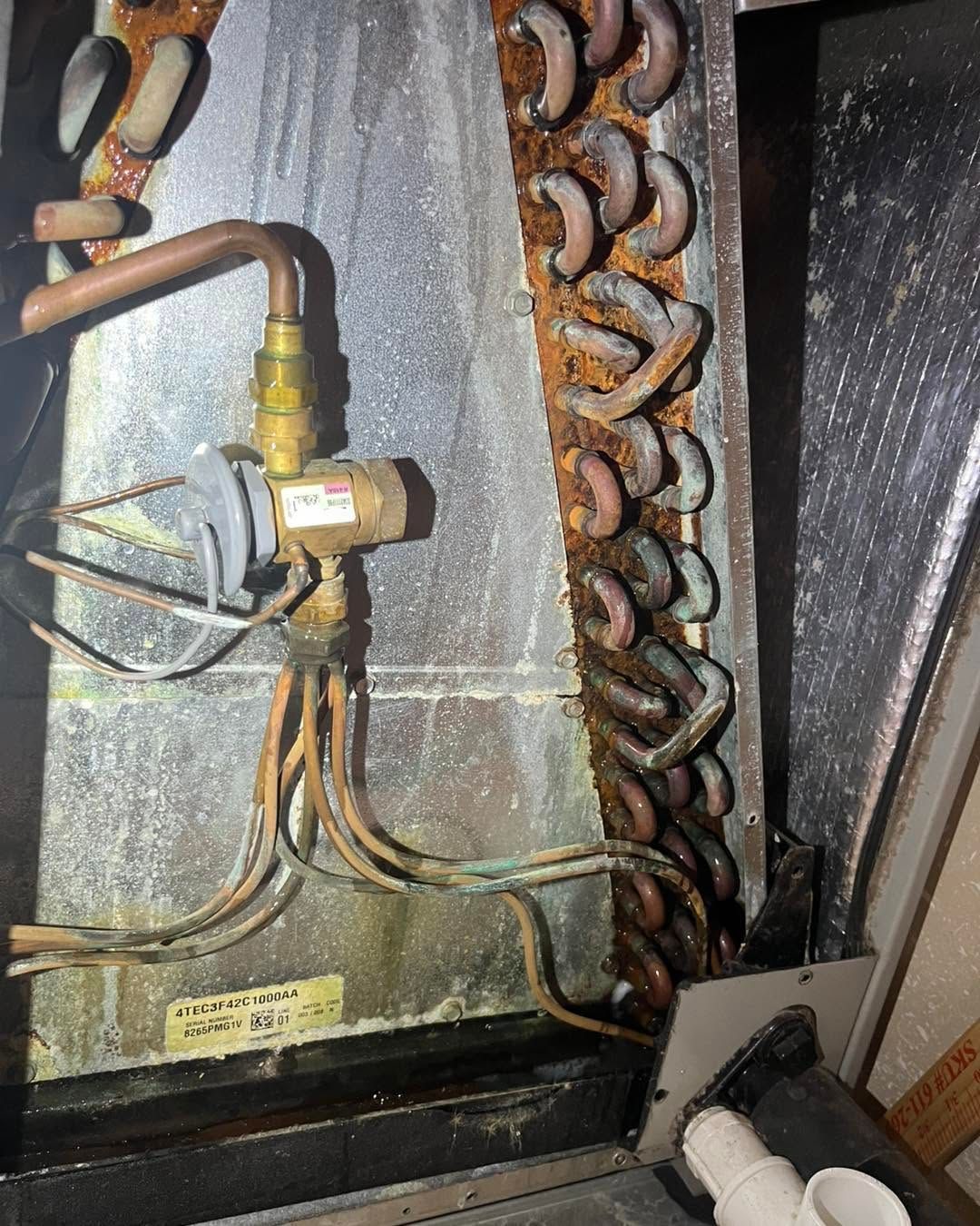 Rusty HVAC valve and pipes inside a dark mechanical unit, with coils and a motor visible.